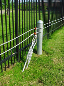 Tall black fence with a vehicle catch cable system shown in the grass in front of it